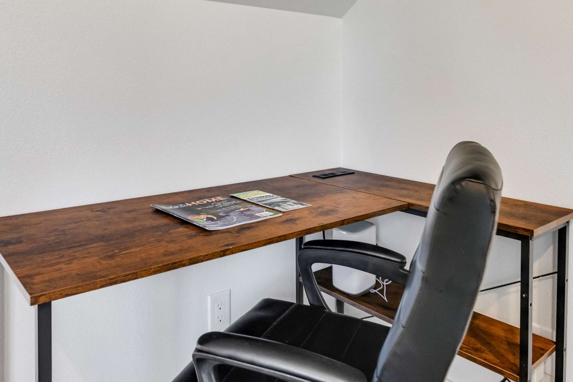 A workspace with a wooden desk, a black office chair, and a magazine on the desk.