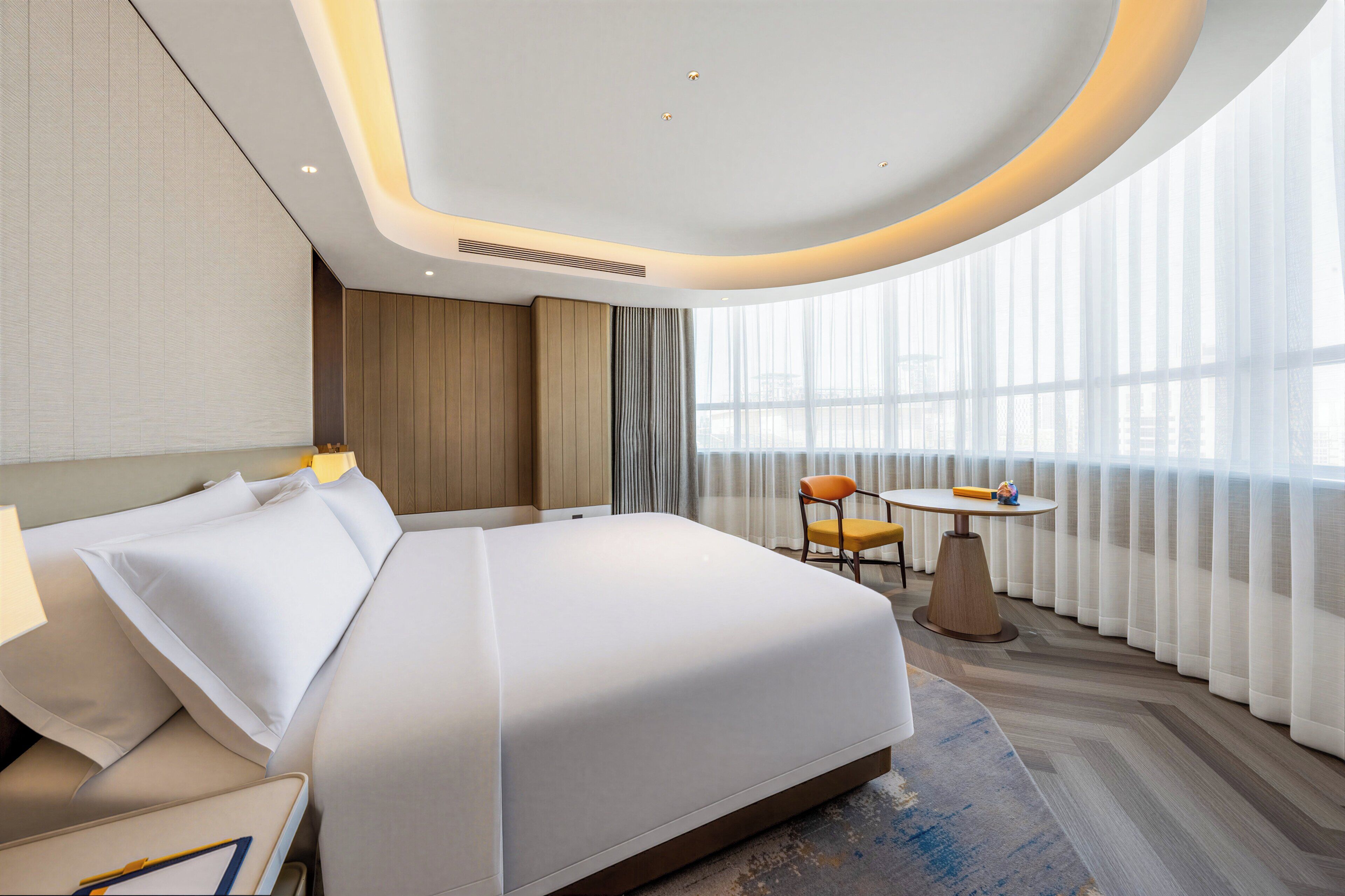 A modern hotel room with a large bed, a small table, and a chair.