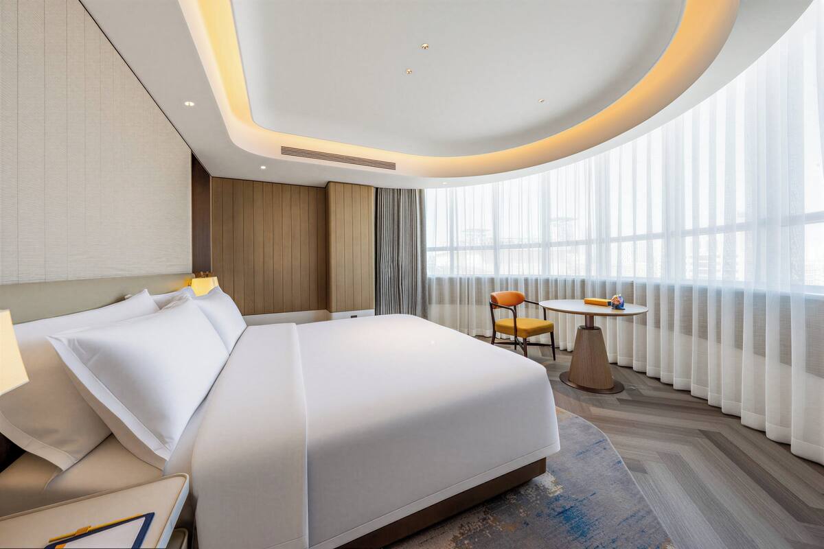 A modern hotel room with a large bed, a small table, and a chair.