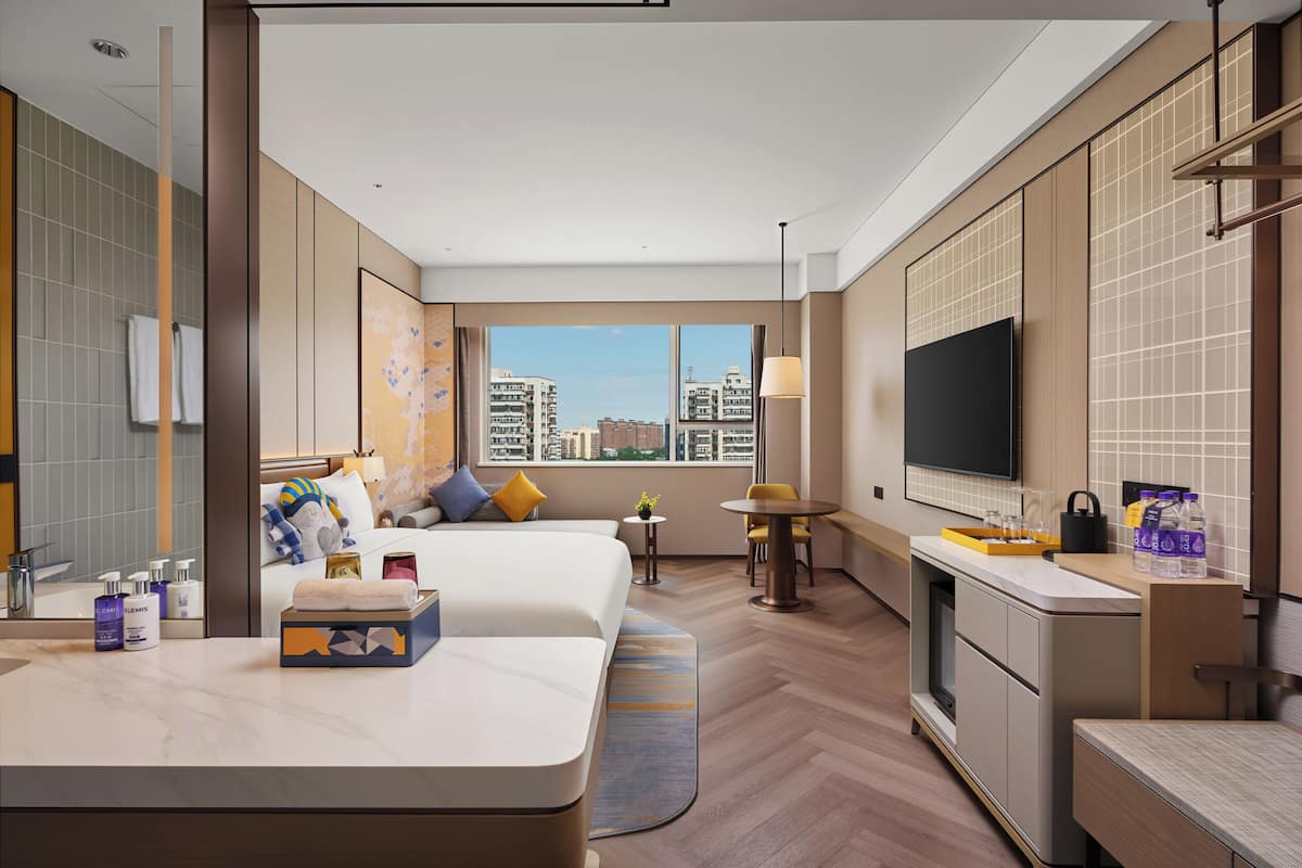 A hotel room with a bed, a desk, a TV, and a view of the city.