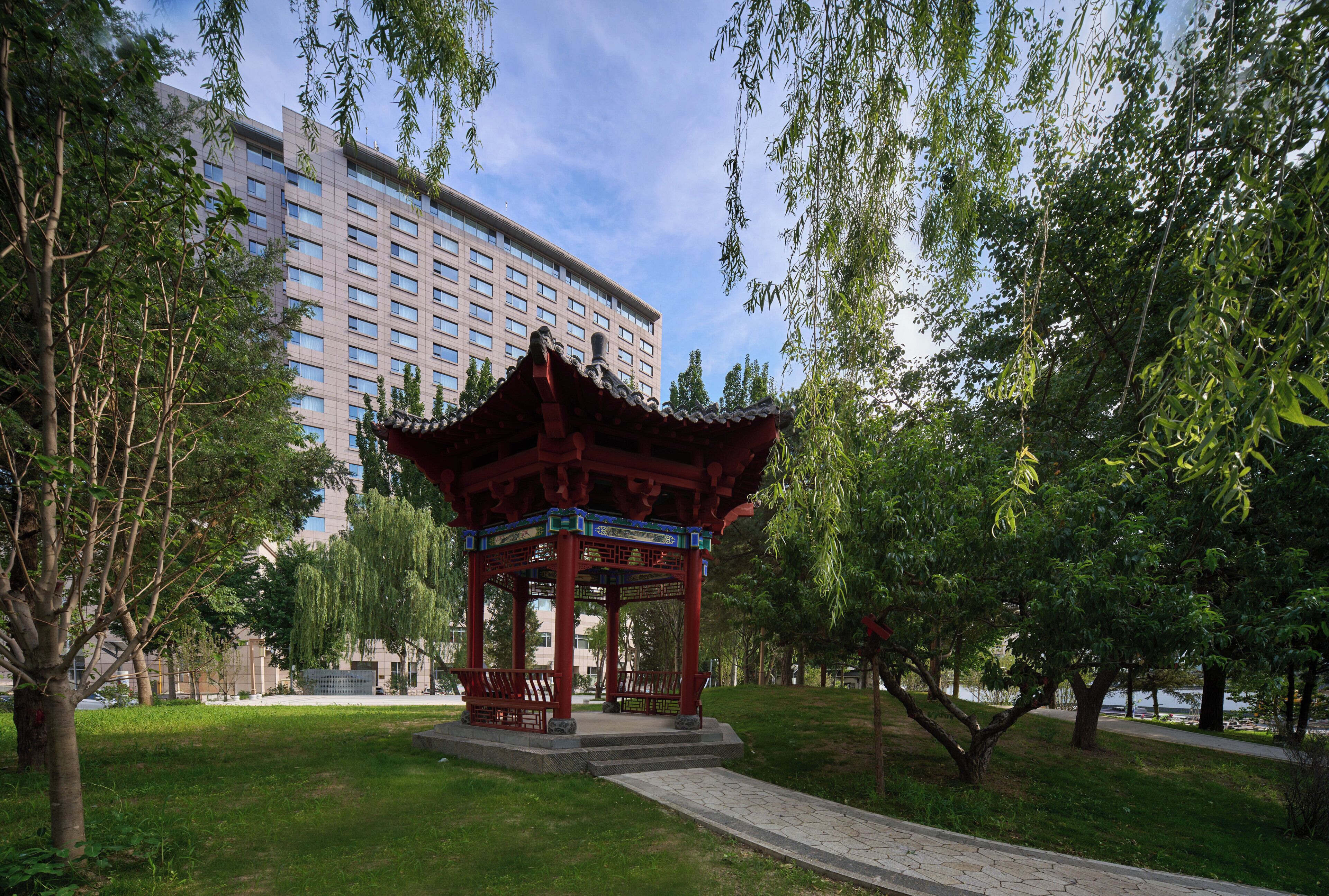 A traditional pavilion in a park with a modern building in the background.
