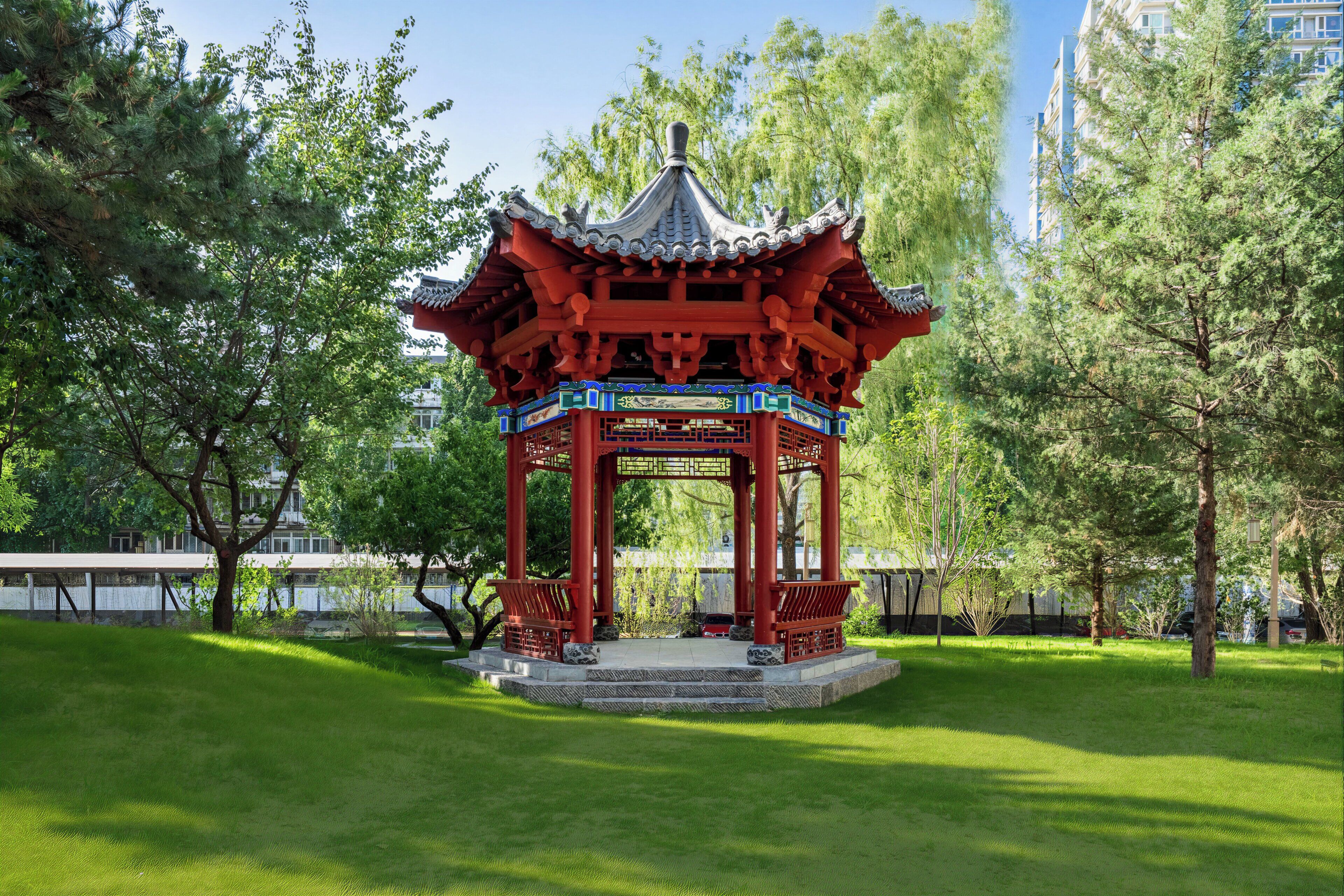 A traditional red pavilion in a park with green grass and trees.
