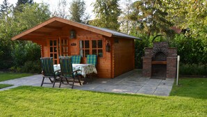 Eine Holzhütte mit einer Terrasse, zwei Stühlen, einem Tisch und einem Kamin aus Ziegelsteinen.
