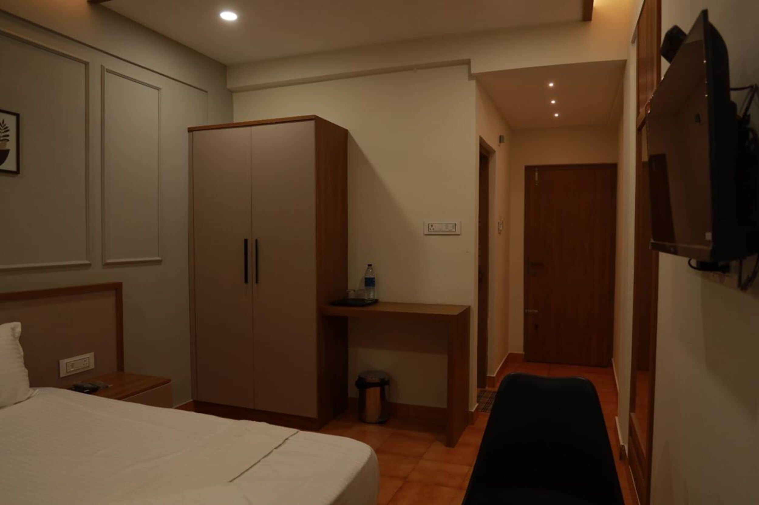 A hotel room with a bed, a wardrobe, a desk, a chair, and a television.