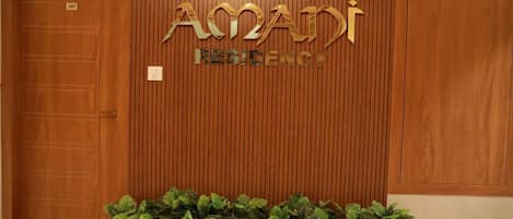 A reception area with a wooden panel wall, a sign reading "AMANDI RESIDENCY," and a potted plant in the foreground.