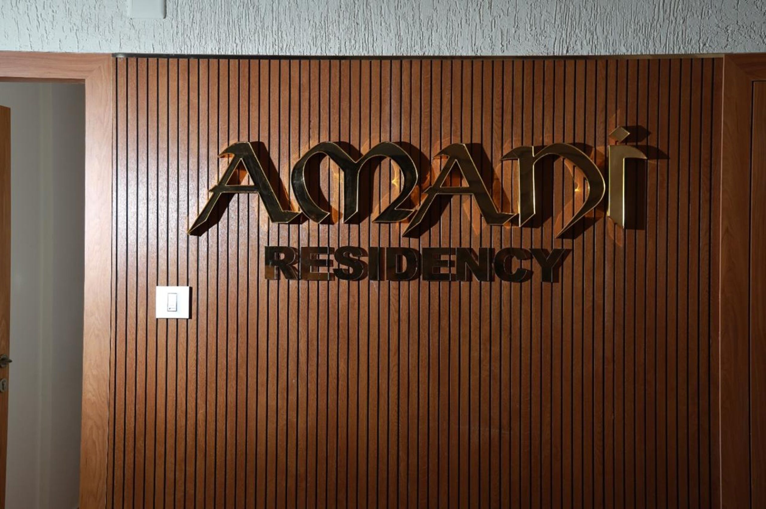 A wooden wall with the text "AMADI RESIDENCY" in a metallic finish.