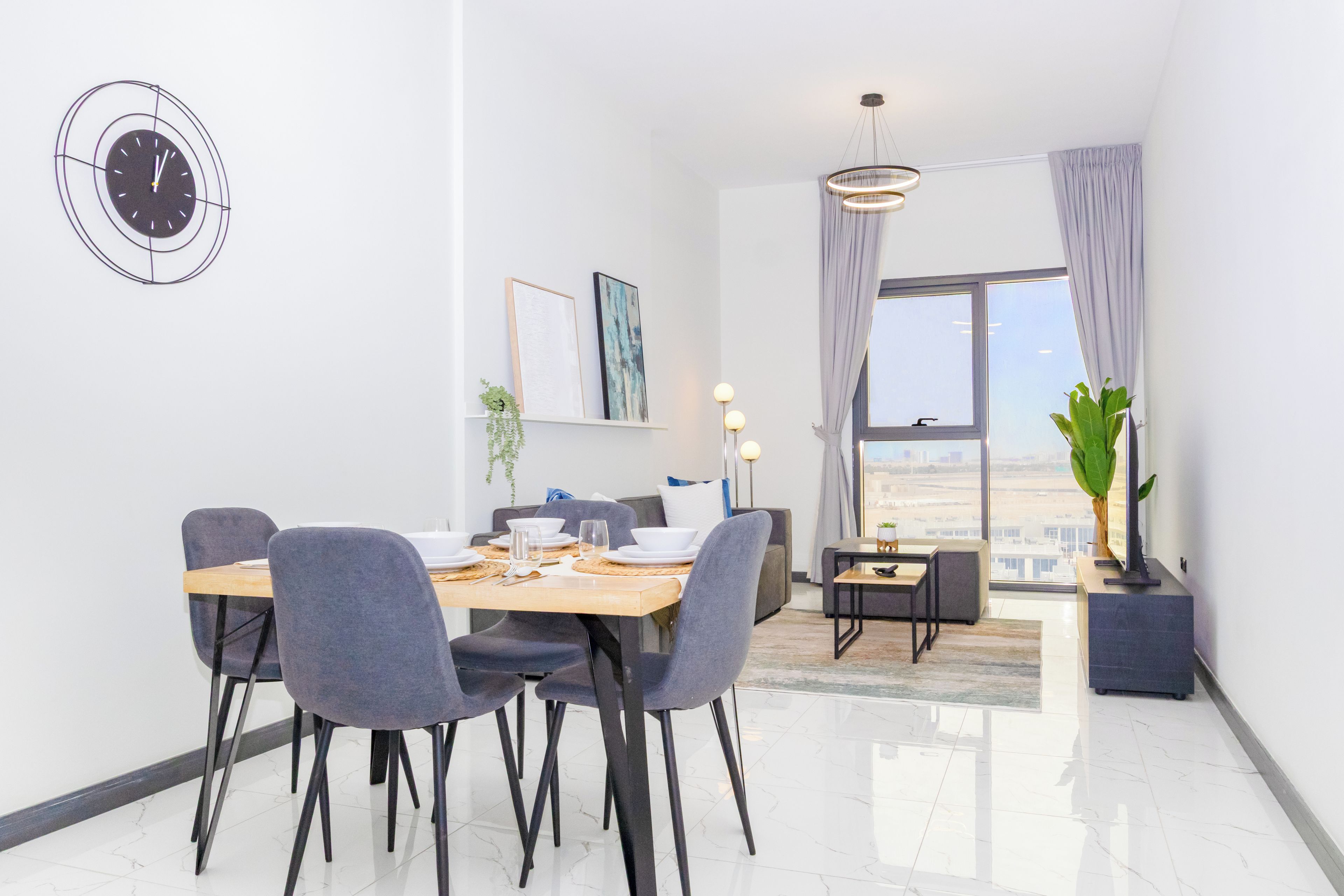A modern dining area with a wooden table, grey upholstered chairs, and a wall-mounted clock.