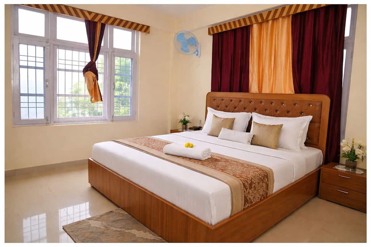 Ein Schlafzimmer mit einem großen Bett, einem Nachttisch, einem Fenster mit Vorhängen und einem Wandventilator.