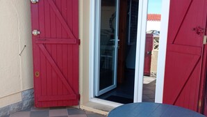 A patio with a checkered floor, a round table, and a red gate. - Cosy Santa 4 PERS (Le Barcarès)