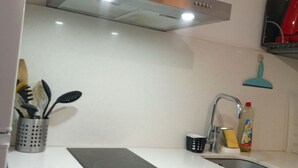 A kitchen with a stainless steel range hood, a sink with a faucet, and a countertop with a cutting board. There are cabinets below the countertop and a plant on the range hood. - Cosy Santa 4 PERS (Le Barcarès)