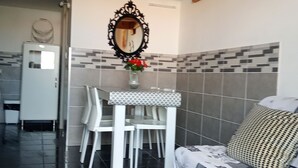 A dining area with a white table and chairs, a mirror above, and a tiled backsplash. - Cosy Santa 4 PERS (Le Barcarès)