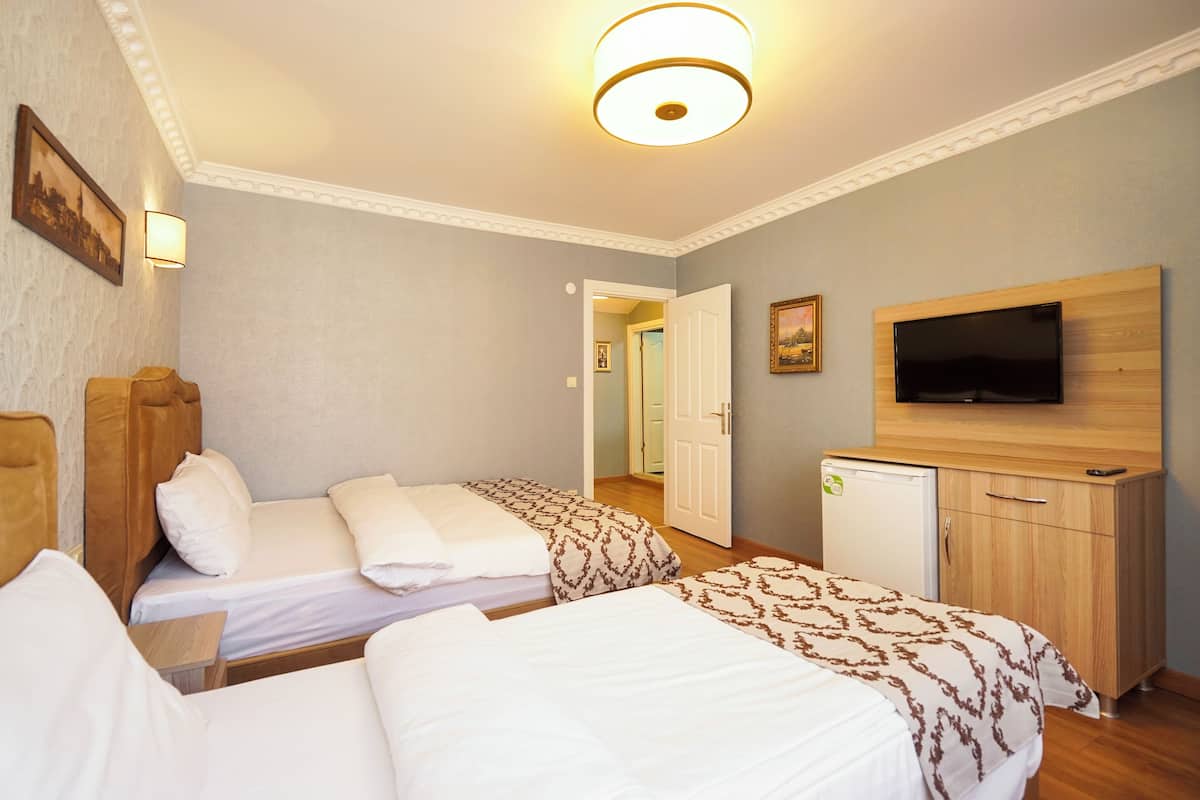 A hotel room with two beds, a television, a small refrigerator, and a door leading to another room.
