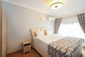 A hotel room with a large bed, a nightstand, a wall-mounted air conditioner, and a window with curtains.