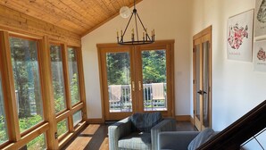 A spacious living room with a high ceiling, large windows, a chandelier, and a view of the outdoors.