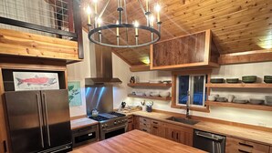 A modern kitchen with wooden cabinetry, a stainless steel refrigerator, a large island, and a hanging light fixture.