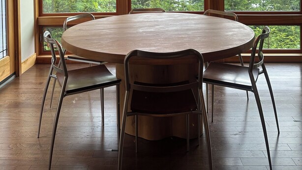 A wooden dining room with a round table and chairs, large windows with a mountain view, and a chandelier.