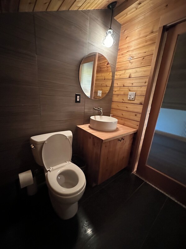 A modern bathroom with a wooden vanity, a round mirror, and a toilet.