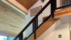 A spacious living area with a wooden staircase, two armchairs, and a large window providing natural light.