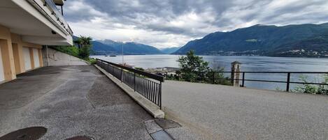 A waterfront property with a balcony overlooking a lake, mountains in the background, and a building with a flat roof.