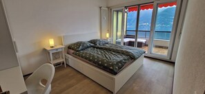 Ein Schlafzimmer mit Bett, Nachttisch mit Lampe, Stuhl und Meerblick vom Balkon.