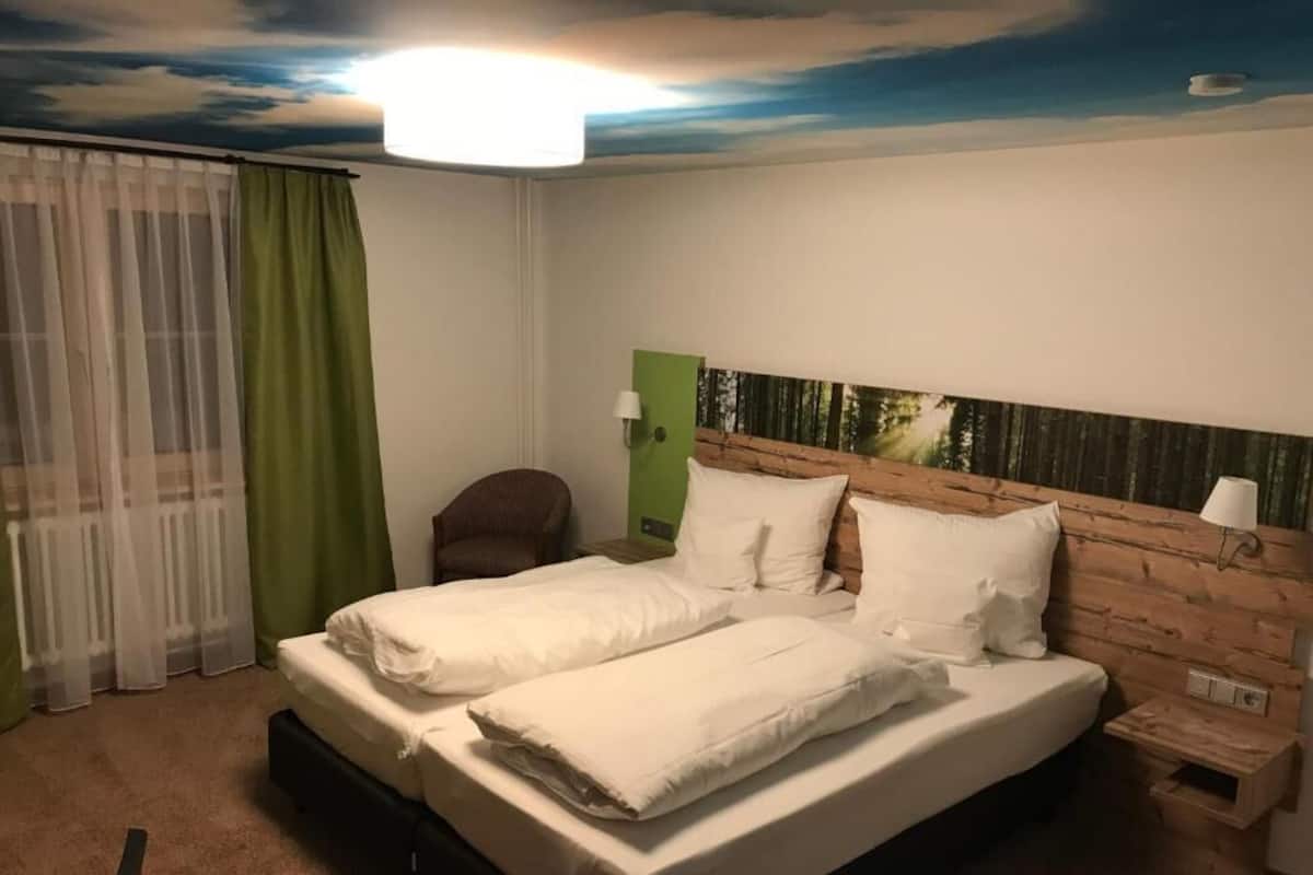 Una cama doble con sábanas blancas, cabecera de madera, pared de acento verde y un mural en el techo.