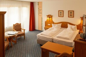 Hotelkamer met een tweepersoonsbed, een bureau met stoel, een klein tafeltje en een televisie.