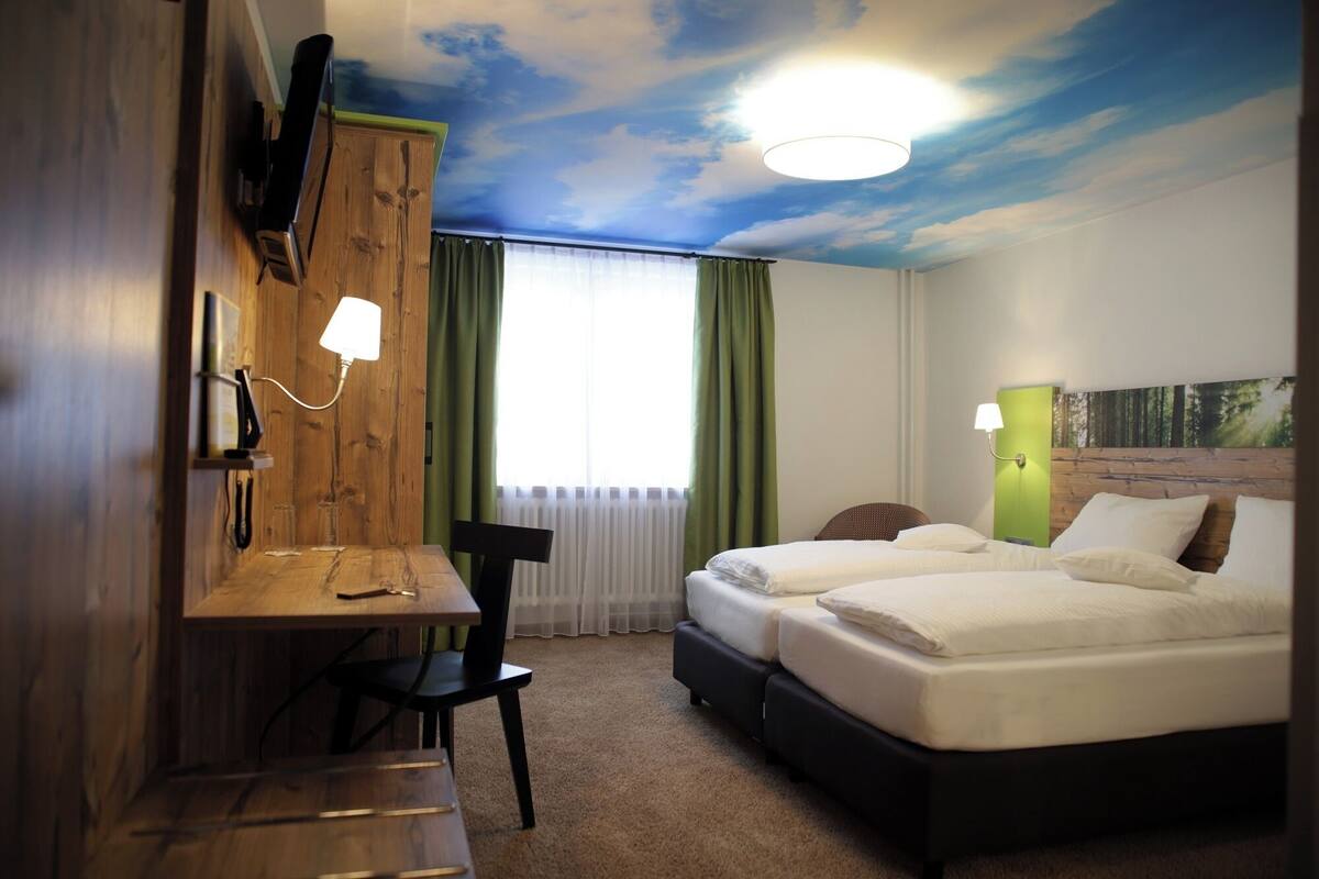 Una habitación de hotel con una cama, un escritorio, una silla y un mural en el techo.
