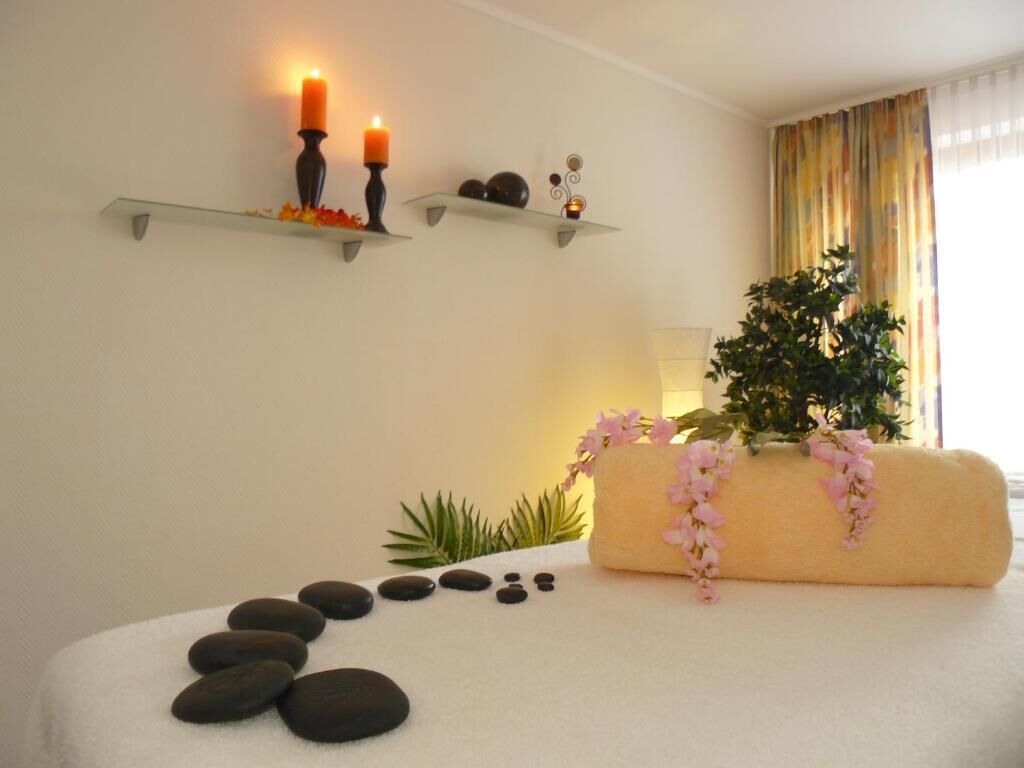 Une salle de spa avec une table de massage blanche, des bougies, une plante et une étagère ornée d’objets décoratifs.