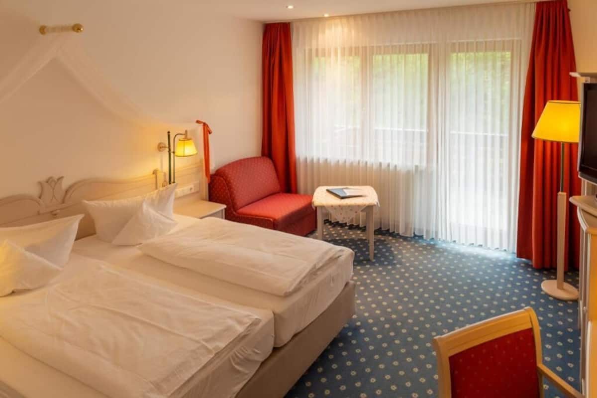 Una habitación de hotel con una cama doble, un sillón rojo, una mesita y un televisor.