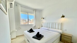 Ein Hotelzimmer mit einem großen Bett, einem Fenster mit Blick auf Gebäude, einem Nachttisch mit Lampe und einem Holzbeistelltisch.
