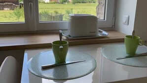 A dining table with two green placemats, a green mug, and a toaster on a windowsill.