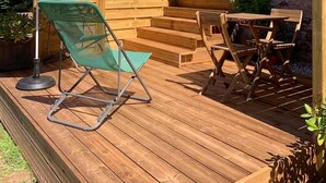 A wooden deck with outdoor furniture, including a red umbrella, a green chair, and a wooden table.