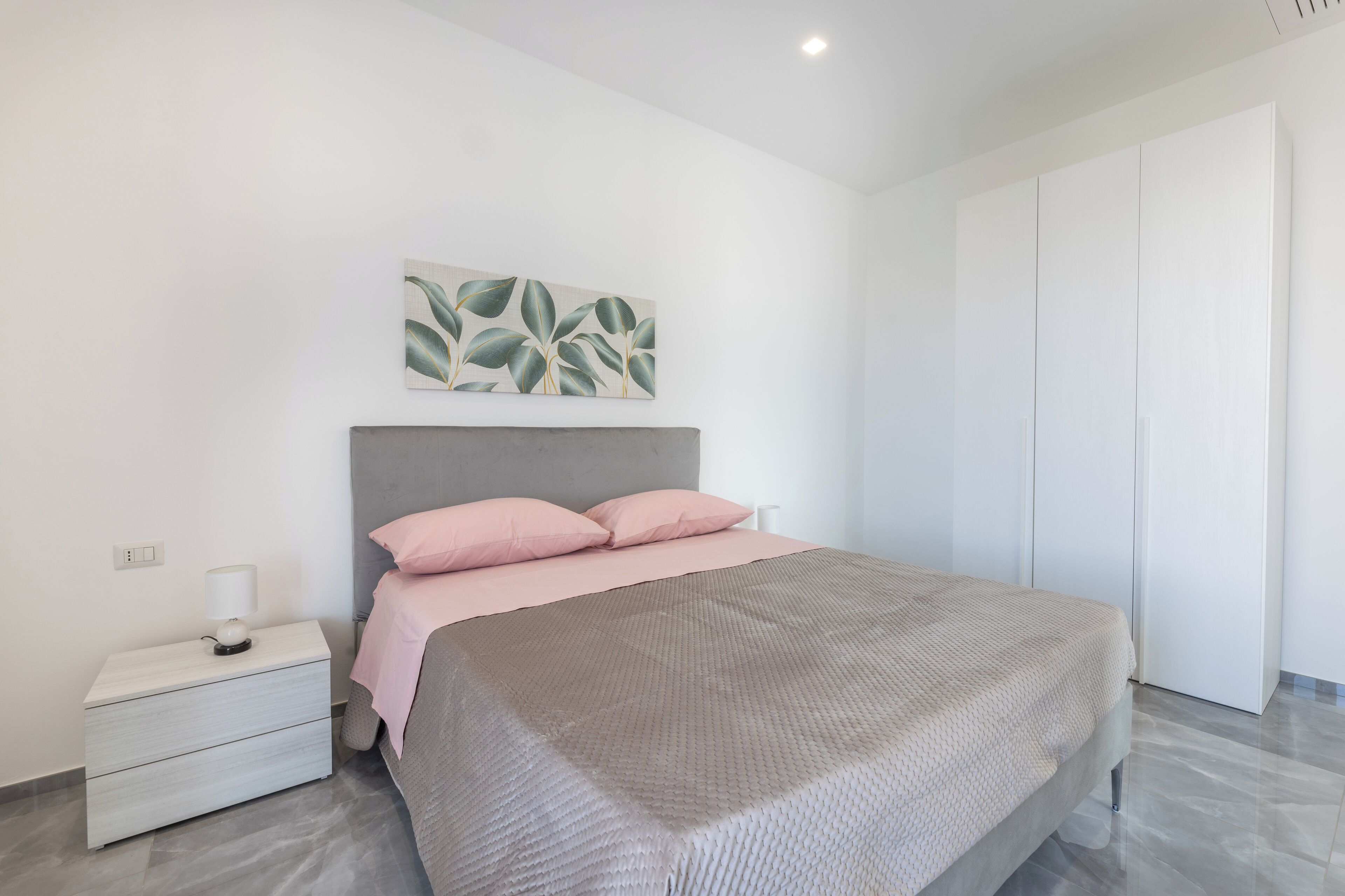 A modern bedroom with a large bed, a nightstand, a wall-mounted lamp, and a wardrobe.