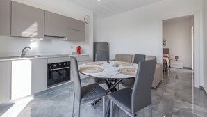 A modern kitchen with grey cabinets, a built-in oven, and a dining area with a marble table and grey chairs.