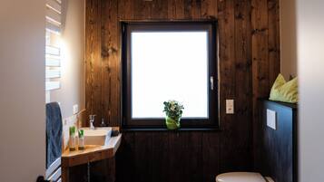 Een badkamer met een houten wand, een raam, een wastafel, een toilet en een plant in een pot.