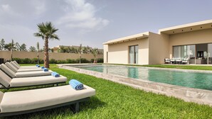 Zona de piscina amb gandules i un edifici modern amb grans finestres.
