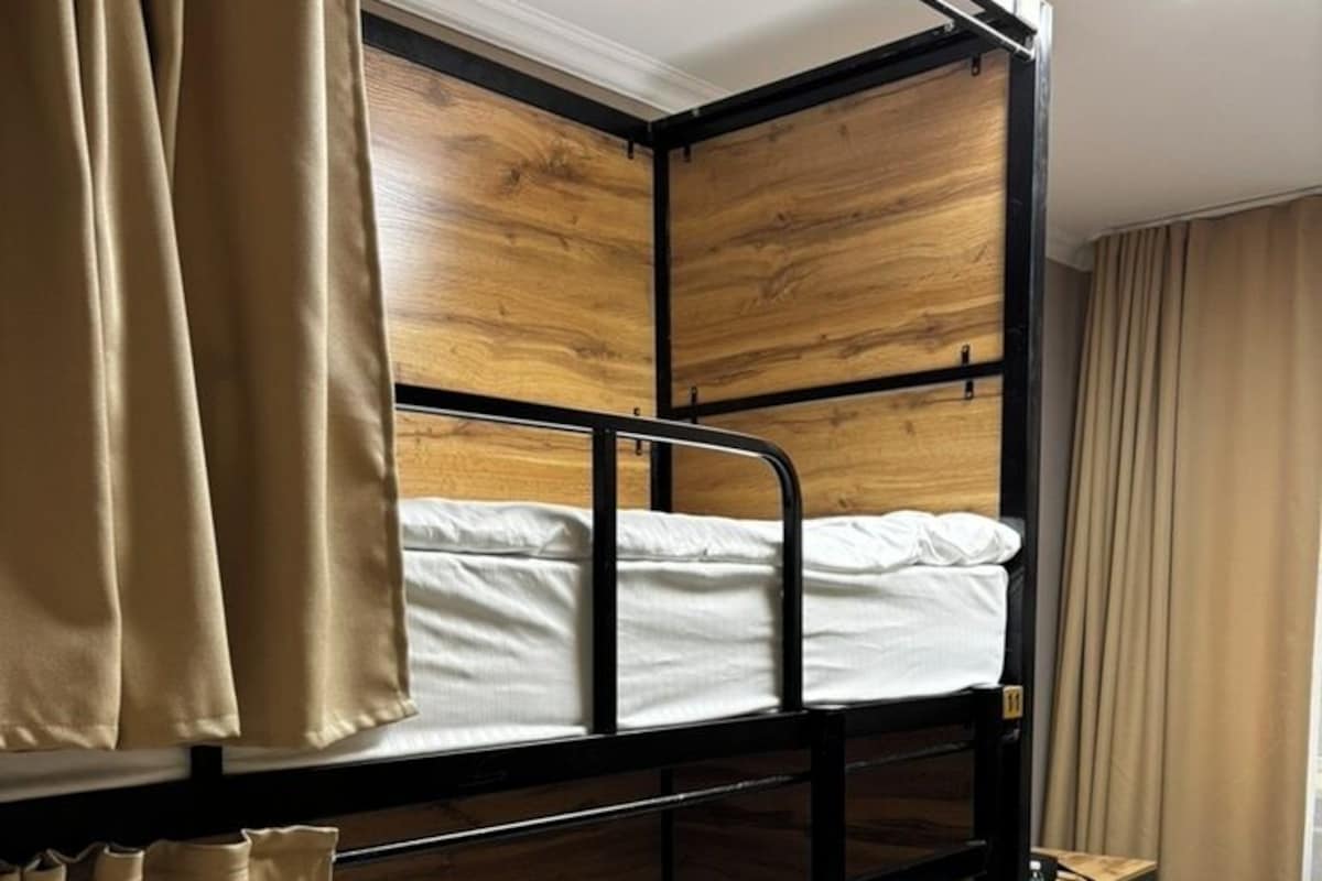 Un lit superposé avec une tête de lit en bois, une petite table et des rideaux beiges.