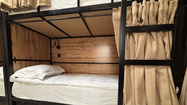 A bunk bed with a wooden headboard, a white mattress, and beige curtains. - Halo.Hostel (Bishkek)