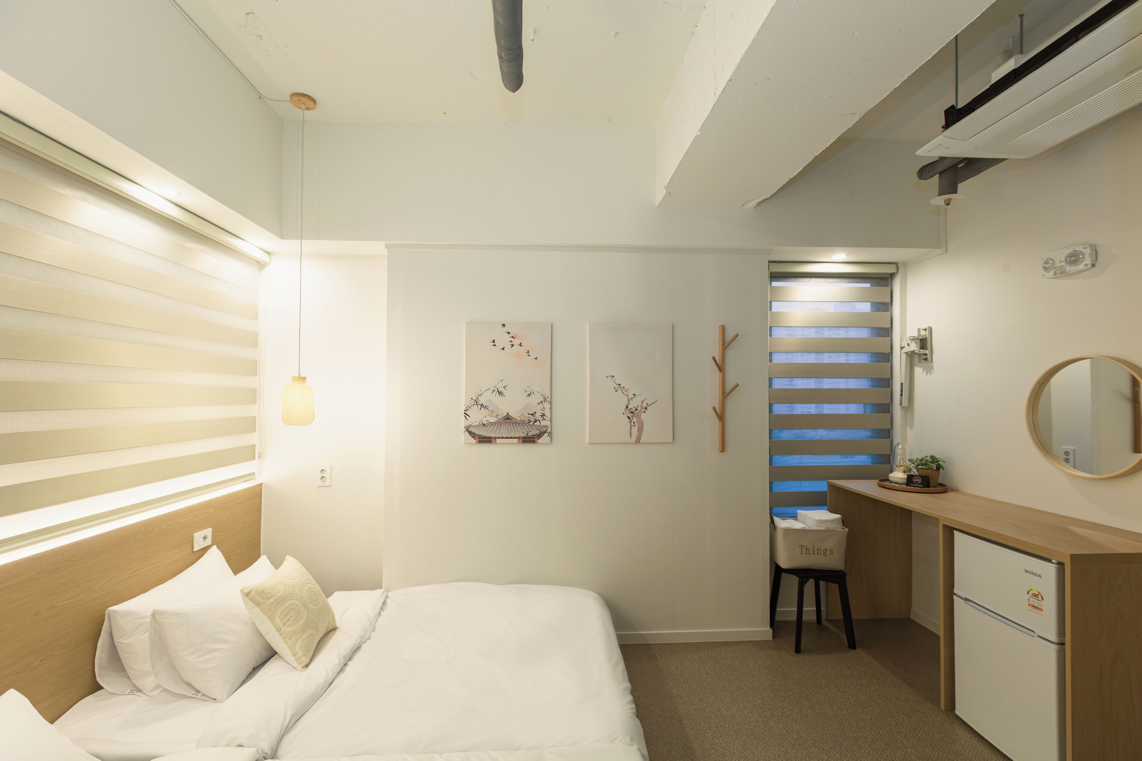 A bedroom with a bed, a desk, a chair, a small refrigerator, and wall-mounted artwork.