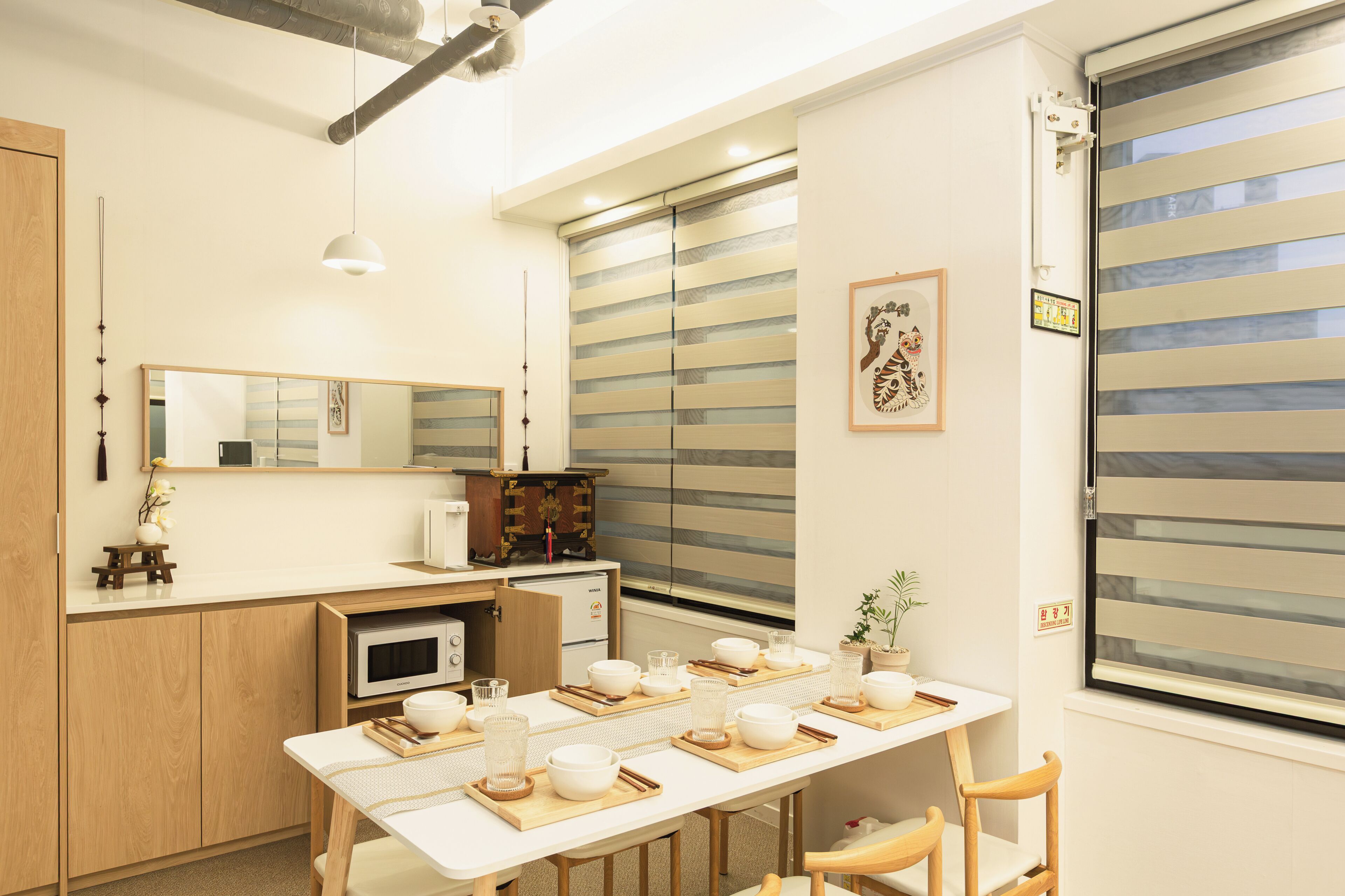 A compact kitchen with a microwave, a small refrigerator, and a dining table set with bowls and glasses.