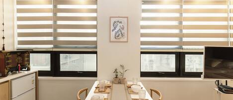 A dining area with a long table, chairs, a refrigerator, and a television on a stand.