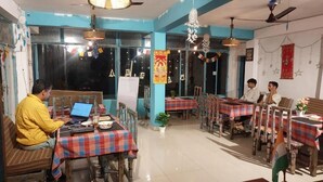 Restaurante com mobiliário de madeira, mesas cobertas por toalhas quadriculadas e uma grande janela ao fundo.