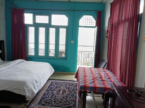 A room with a bed, a table, and a window with curtains. - Hotel Freedom Palace (Dharamshala)