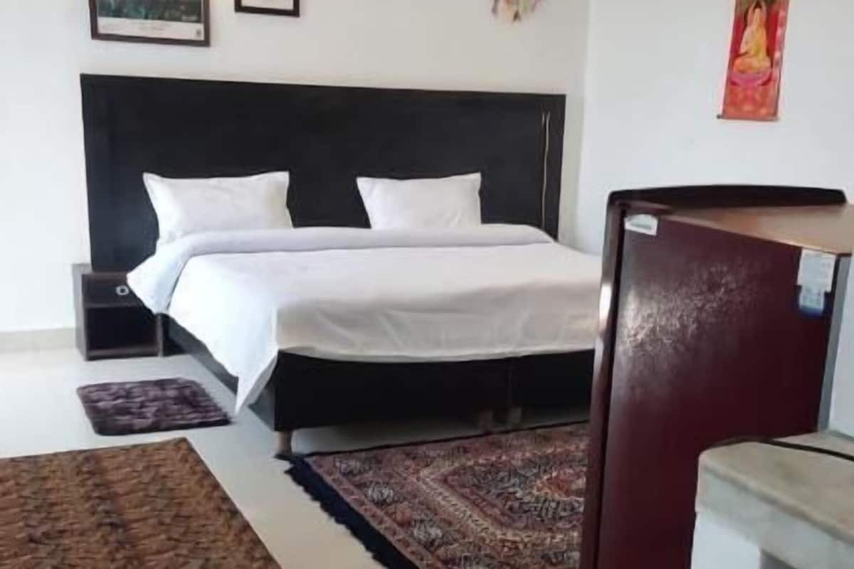 A bedroom with a bed, a desk, a chair, a ceiling fan, and artwork on the walls.