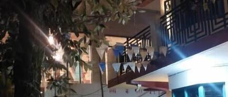 A building with a staircase leading to a balcony, surrounded by greenery and decorated with triangular flags.