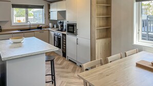 Eine moderne Küche mit Kochinsel, integrierten Geräten und einem Essbereich mit Holztisch und Stühlen.