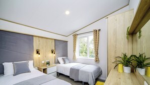 Ein Schlafzimmer mit zwei Betten, Nachttischen, einem Fenster mit Vorhängen und einer Zimmerpflanze.