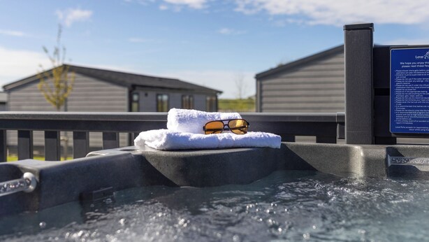 Un jacuzzi con una toalla y gafas de sol encima, una terraza de madera y un cartel con texto.