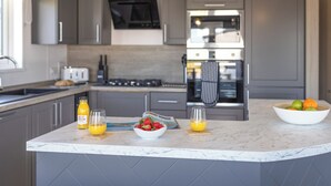 Una cocina moderna con armarios grises, una isla central con cestos de fruta y un horno empotrado.
