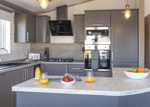 Une cuisine moderne avec des meubles gris, un îlot central agrémenté de corbeilles de fruits et un four encastré.